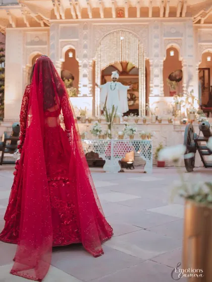 A powerful and emotional shot of the bride in her red lehenga walking towards the groom, who waits with open arms at the mandap.