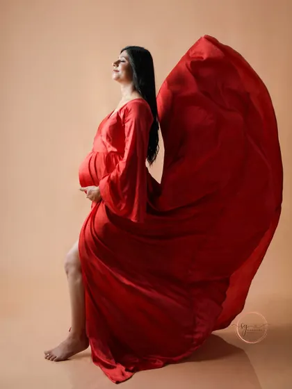 An artistic side profile with the red gown flowing dramatically behind. This shot emphasizes the beauty and power of the pregnancy silhouette.