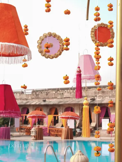 The poolside decor for the Haldi, with hanging lampshades and marigold tassels reflecting in the water. The design utilized every part of the venue to create an immersive experience.