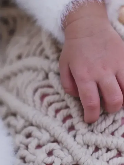 A macro shot of a newborn's hand resting on a textured blanket, emphasizing the smallness and perfection of their fingers.