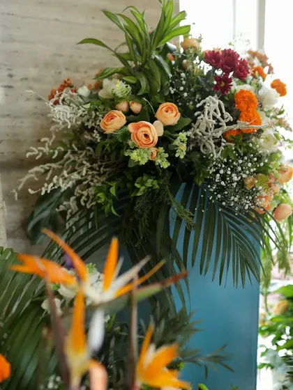A lush floral arrangement with peach roses, Birds of Paradise, and tropical leaves, adding a burst of color to an event entrance.