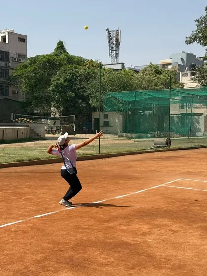 A female player in the middle of her service motion during an AITA tournament. Her form demonstrates a focus on technique and power generation.