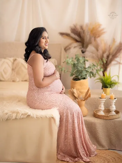 A serene portrait of a mom-to-be in a pink sequin gown, seated on a fur-covered bed in our cozy boho setup.