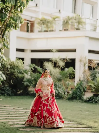 A full-length portrait of the bride in her magnificent red lehenga, walking through a beautiful garden.