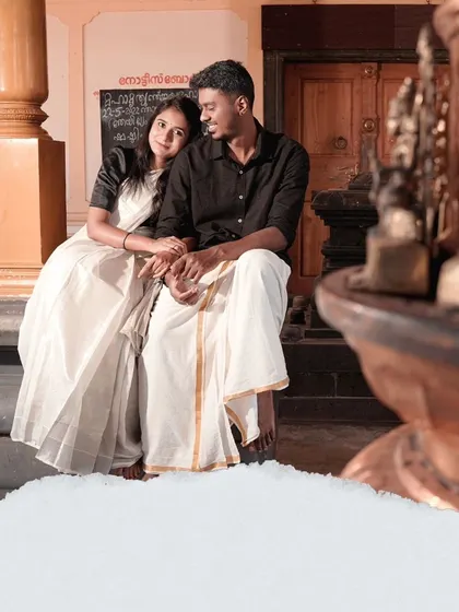 An intimate moment captured at a traditional Kerala temple, with the couple dressed in classic white and black attire, reflecting the local culture.