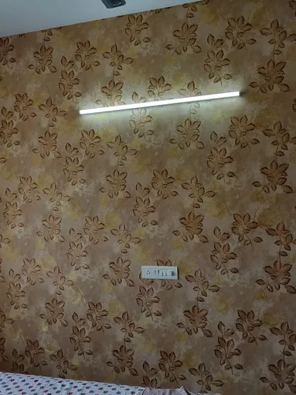 A bedroom wall with a dark, textured wallpaper featuring a subtle leaf pattern. The design adds depth and a touch of sophistication.