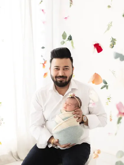 A proud father holding his newborn daughter. The floral background adds a touch of softness to this beautiful portrait of a dad's first love.