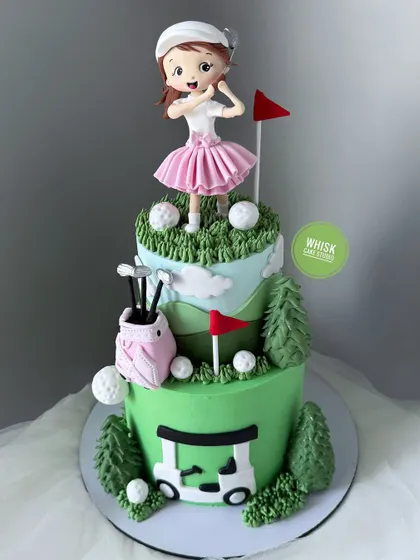 A hole-in-one of a cake for a golf player. This two-tiered cake is decorated with a golf course theme, including a handcrafted female golfer, a golf cart, and clubs.
