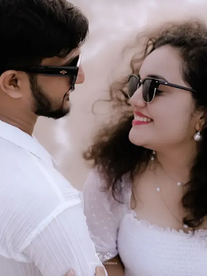 A close-up of the couple smiling at each other, their sunglasses adding a cool, stylish vibe to their beach shoot.