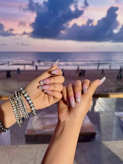 Vacation nails on point. This beautiful shot captures a subtle glitter ombré against a stunning beach sunset, proving that great nails are the best travel accessory.