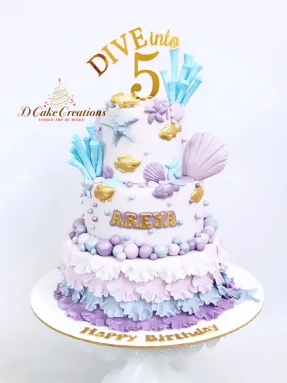 "Dive into 5" with this beautiful two-tier underwater-themed cake for Areya. The design features pastel ruffles, edible sea shells, and crystal-like sugar shards.