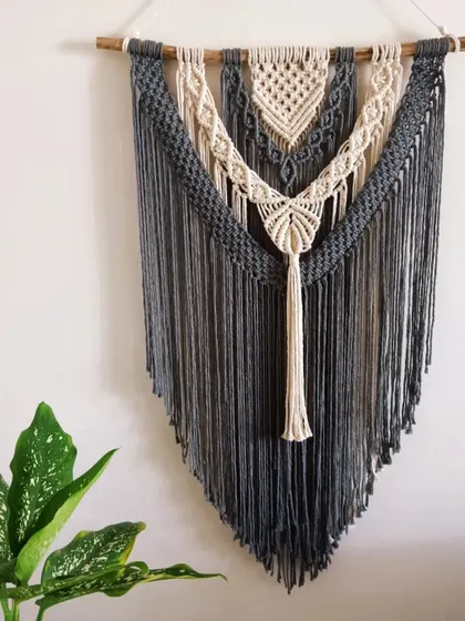 The finished grey and off-white macrame tapestry hanging on the wall. It's about 2.25 by 4 feet, a great size for a living room or bedroom. Customization is always available!