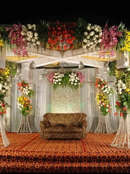 A classic wedding reception stage design. We use a combination of colorful floral arrangements on pedestals and a beautifully draped backdrop to create a timeless and elegant setting.