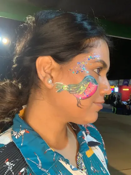 A sweet little bird painted on a client's cheek, surrounded by a spray of glitter.
