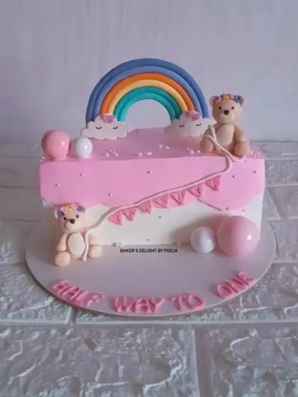 A pink and white half-birthday cake with two adorable teddy bears and a rainbow. This design is perfect for celebrating a little one being "halfway to one."