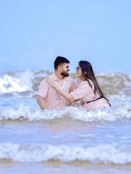 Fun and playful pre-wedding photography on the beach. This shot captures a couple enjoying the waves in our stylish, matching striped casual wear, perfect for a destination shoot.