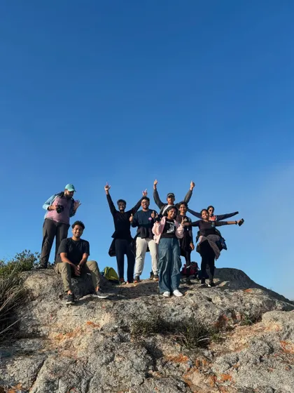 Students cheering at the top of a rock, celebrating their achievement together. These moments of shared victory are what build strong teams.