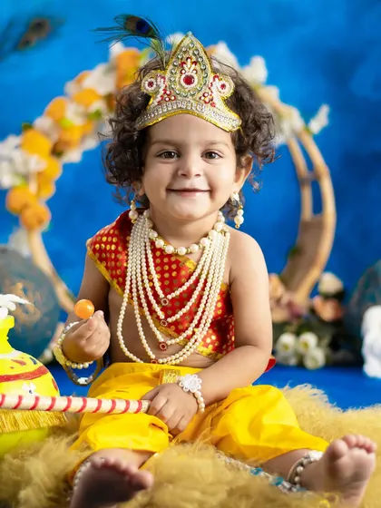 This smiling little Krishna is holding a sweet treat, adding an extra layer of cuteness to the photo.
