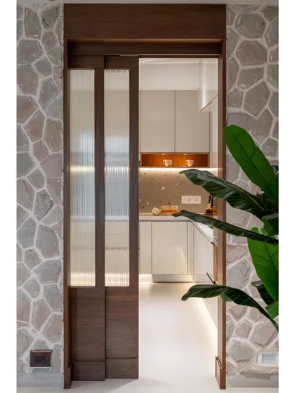 A view from the living room into the kitchen, showing the beautiful contrast between the rough stone wall and the sleek, modern kitchen beyond.