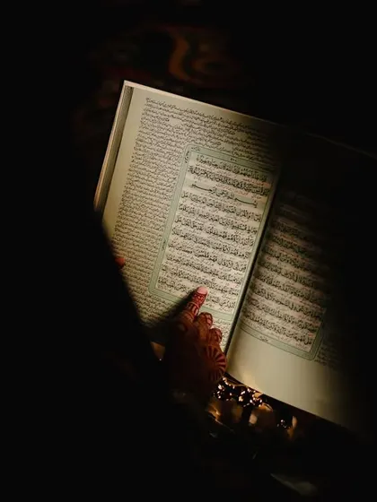 A close-up shot of a hand on the Quran, with light falling only on the sacred text, creating a deeply spiritual and focused image.
