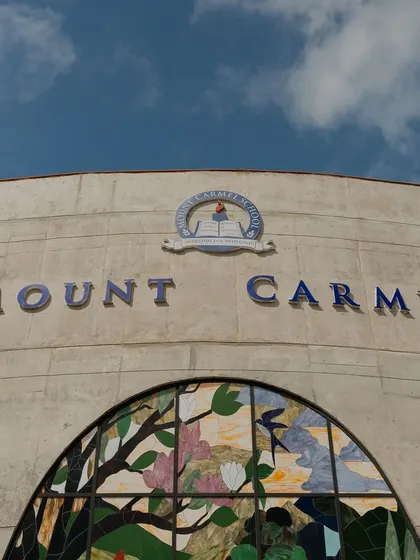 The main entrance facade of Mount Carmel, featuring exposed concrete and a large stained-glass mural. This combination of raw materiality and artistry sets the tone for the creative and spiritual ethos of the educational space within.