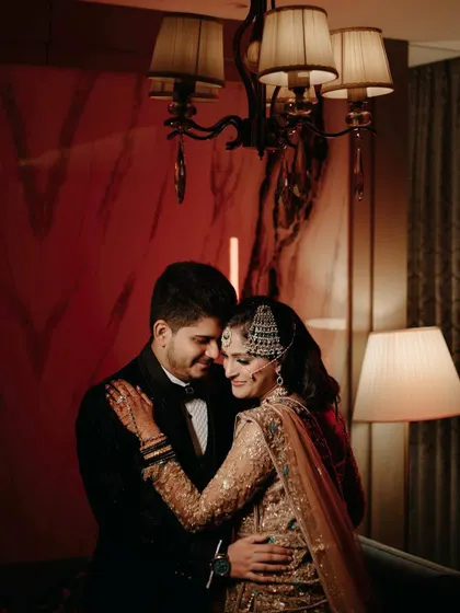 An elegant embrace under the soft light of a chandelier. The bride's traditional jewelry and the groom's classic tuxedo create a timeless and sophisticated portrait.