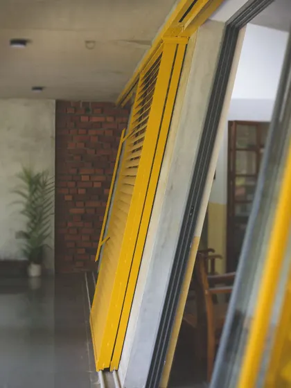A close-up of the angled, yellow louvered shutters at "Aamra." This detail shows the precision in construction and the pop of color that contrasts with the earthy material palette.