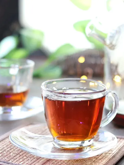 A close-up of one of the glass teacups, focusing on the rich, amber color of the tea. The blurred background keeps the focus entirely on the drink.