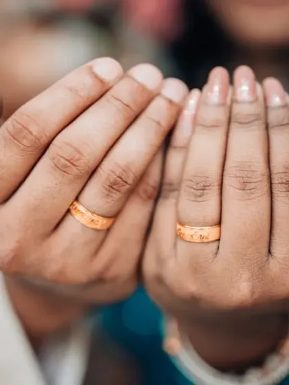 A close-up of the couple's hands held together in prayer, showing their matching gold engagement bands.