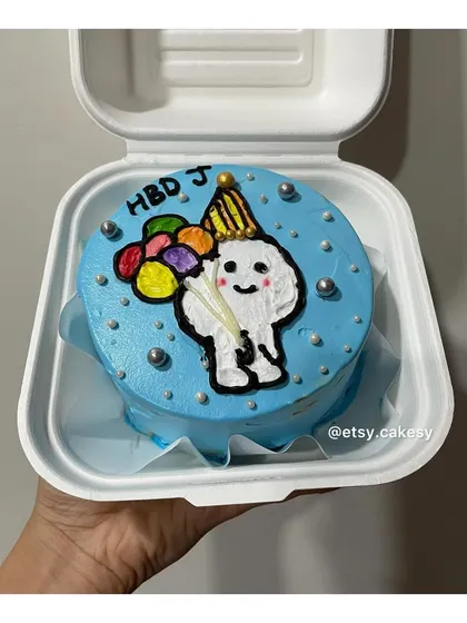 A festive birthday bento cake with a cartoon character holding balloons.