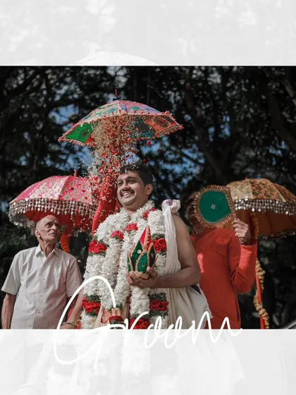 A joyful shot of the groom during his wedding procession, being showered with flowers under colorful umbrellas.