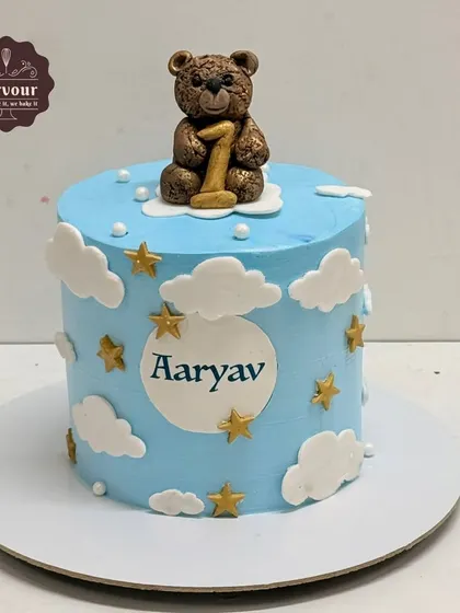 A sweet first birthday cake with a teddy bear on top. This blue cake is decorated with clouds and stars, perfect for a little boy's celebration.