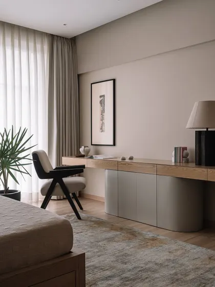 This bedroom features a custom-designed floating desk and storage unit that spans the length of the wall. The curved cabinet doors and light oak finish create a soft, minimalist workspace within the serene bedroom environment.
