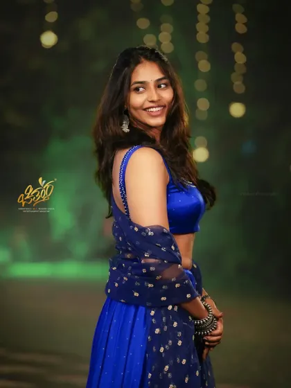 A portrait of actress Sapthami Gowda in a vibrant blue lehenga. The outdoor evening setting with bokeh lights adds a magical quality.