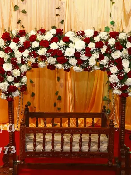 A classic wooden cradle decorated with an arch of red and white roses. This timeless setup is perfect for a traditional naming ceremony or thottil shastra.