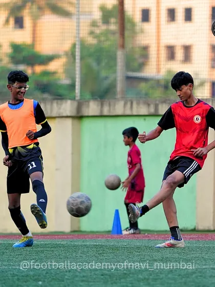 A player in a red bib prepares to strike the ball while his teammate looks on. Practice matches help build chemistry and understanding between players.
