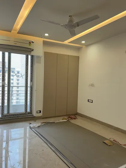 A bedroom during the renovation process, with a newly installed floor-to-ceiling wardrobe and false ceiling. The large window provides ample natural light.
