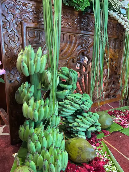 Stacks of green bananas and coconuts placed against a carved wooden backdrop, highlighting the authentic South Indian touches in the decor.