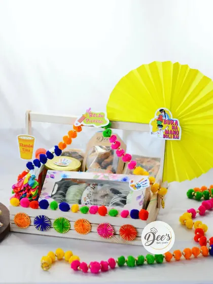 A large wooden tray hamper perfect for Holi celebrations. It's loaded with Chocolate Gujiyas, a Thandai Tea Cake, and other treats, decorated with bright, festive colors.