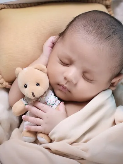 A close-up on the newborn's face as they cuddle a small teddy bear. This intimate shot captures the pure innocence and sweetness of this fleeting stage.
