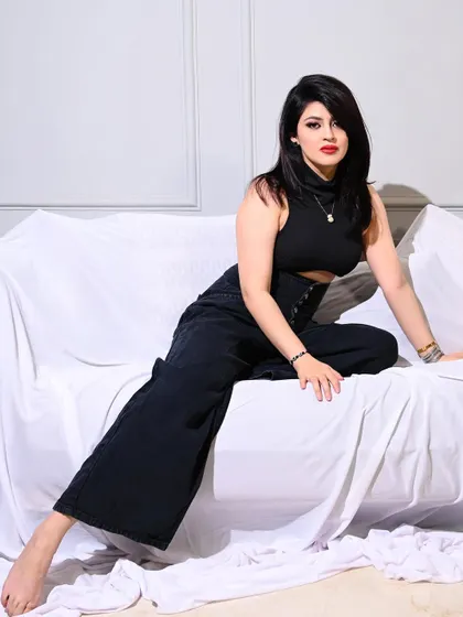 A powerful and edgy shot of a model in an all-black outfit, posing on a white-draped sofa.