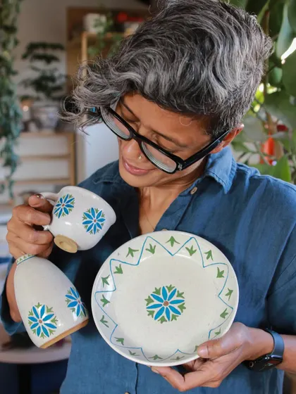 Holding a few pieces from a student's hand-painted collection. The floral motifs are delicate and serene, reflecting the artist's gentle personality.