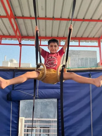 The joy of accomplishment. This young student is holding a challenging straddle pose on the rings.