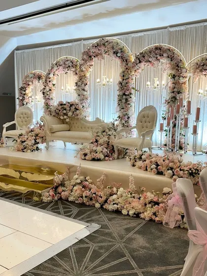 An elegant stage for a Nikkah or Walima, featuring multiple floral arches and classic white furniture.