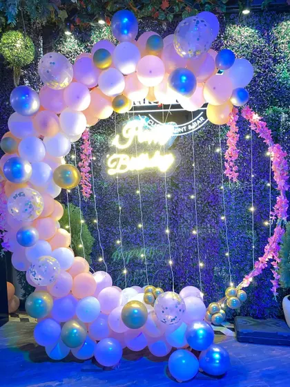 An elegant birthday balloon ring in pastel shades with blue and gold accents, set against a green wall.