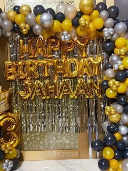 A full view of a black, gold, and silver balloon arch setup for a 13th birthday at home. The shimmer curtain and large crowned number balloon make for a great photo corner.