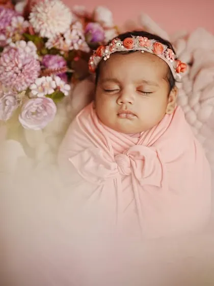 A dreamy, soft-focus shot of a newborn girl surrounded by flowers. The artistic blur in the foreground adds a magical quality to this infant portrait.