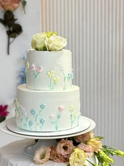 A still shot of the minimal two-tier cake with pastel piped flowers and fresh white roses on top.