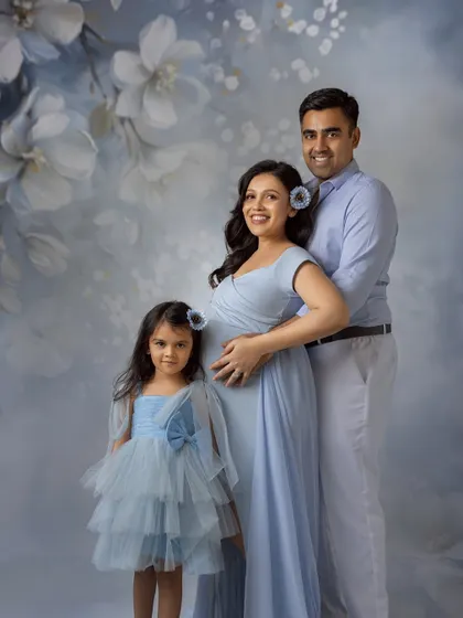 A beautiful family of three, soon to be four. Dressed in coordinating shades of blue, they pose against a lovely floral backdrop for a maternity session that includes their daughter.