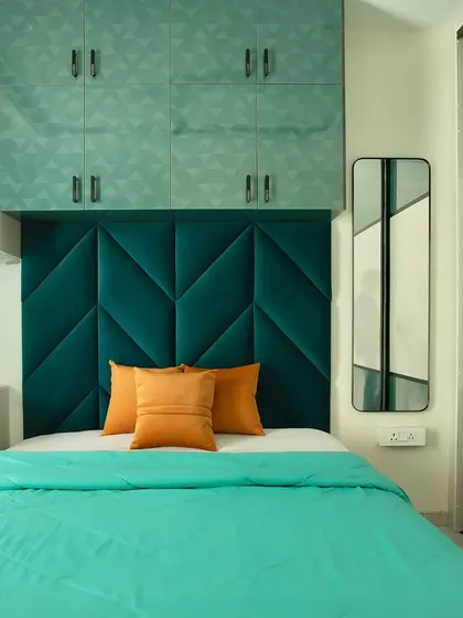 A bold and beautiful bedroom design featuring a deep teal, velvet-tufted headboard and matching geometric-patterned overhead cabinets for extra storage.